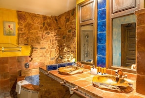 A bathroom with a stone wall, a bathtub, and a sink with a wooden basin.
