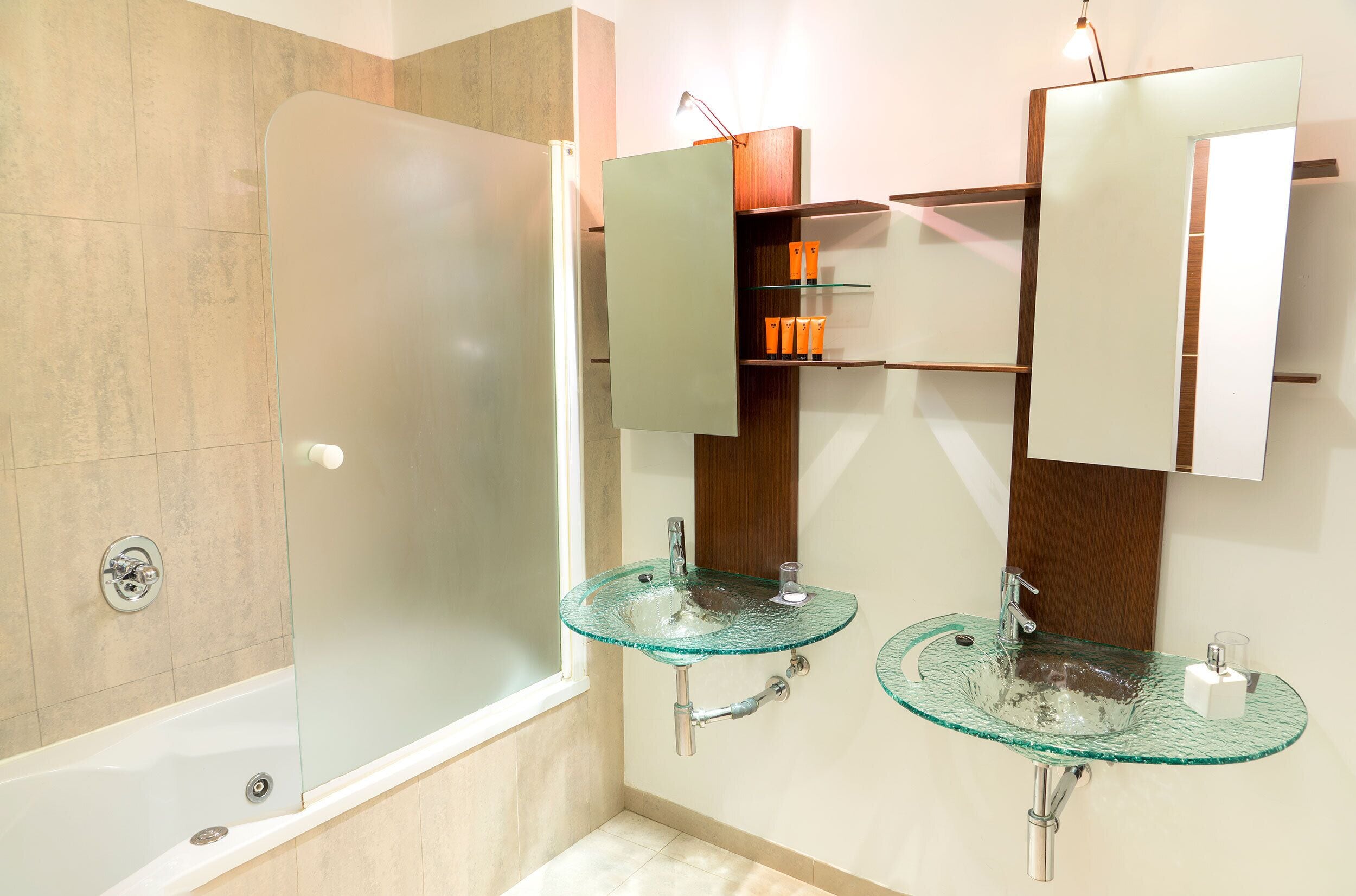 A bathroom with a glass-enclosed shower, two glass sinks, and a wooden vanity with a mirror.