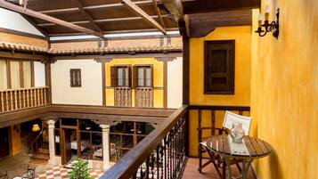 Un patio tradicional con balcón de madera, suelo a cuadros y una mesa con un jarrón.
