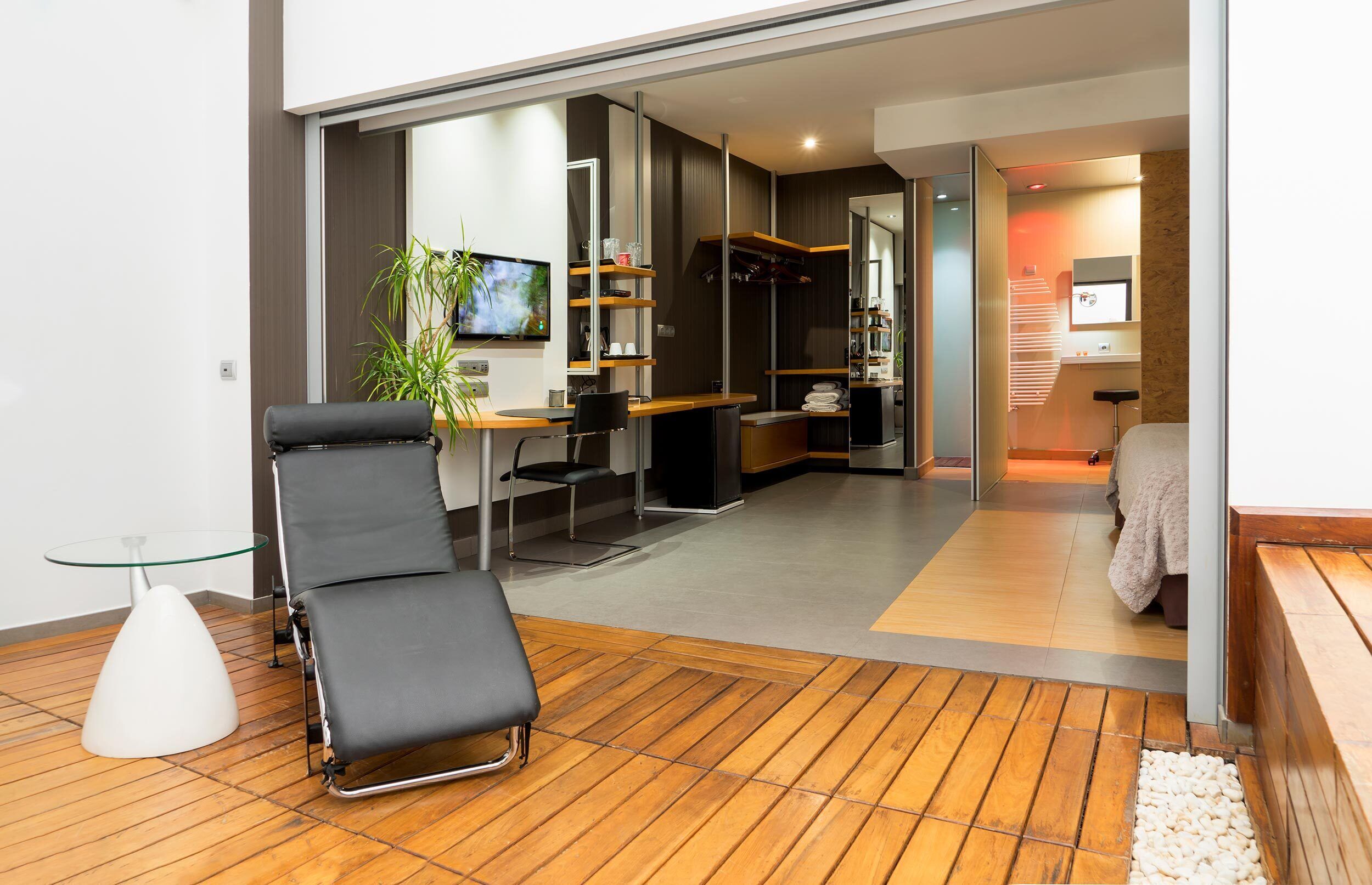 Een moderne woonkamer met een zwarte loungestoel, een glazen salontafel, een televisie en een houten vloer.