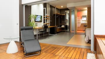 Een moderne woonkamer met een zwarte loungestoel, een glazen salontafel, een televisie en een houten vloer.