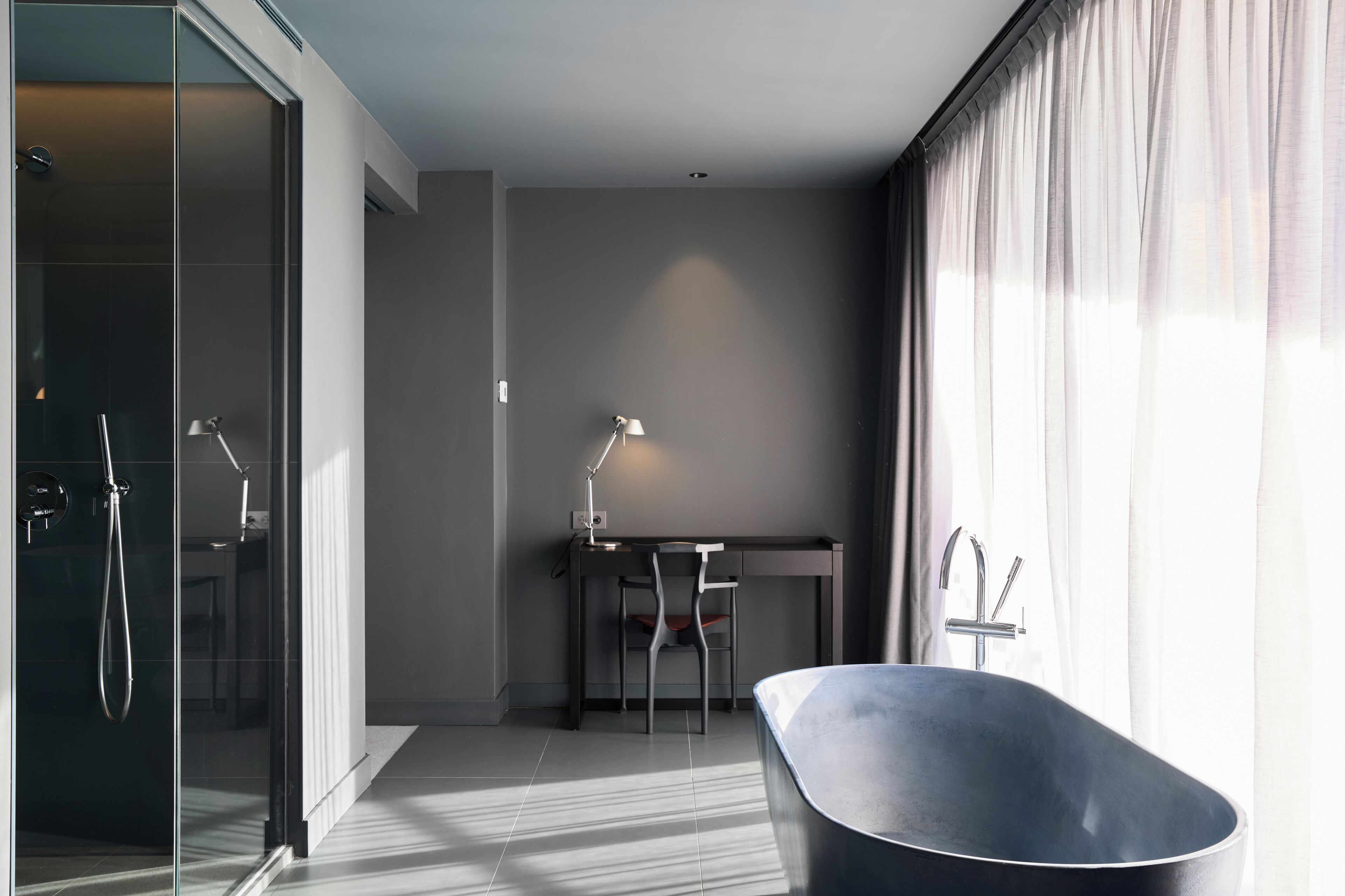 Un baño moderno con una bañera independiente, cabina de ducha de vidrio y un escritorio con silla.