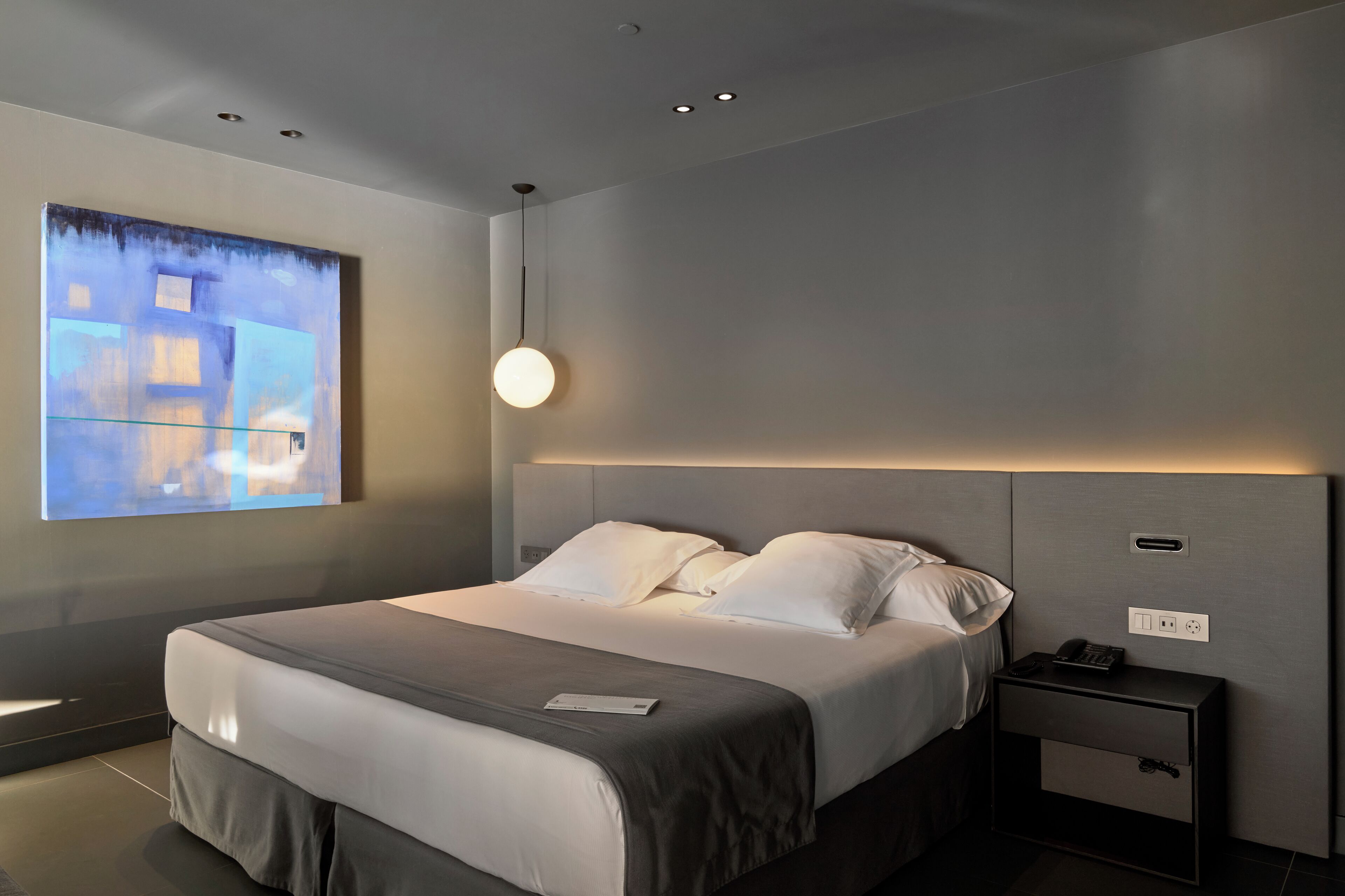 Habitació d'hotel moderna amb un llit gran, una taula de nit i una obra d'art penjada a la paret.
