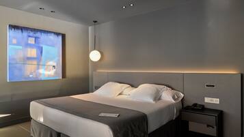 Habitació d'hotel moderna amb un llit gran, una taula de nit i una obra d'art penjada a la paret.