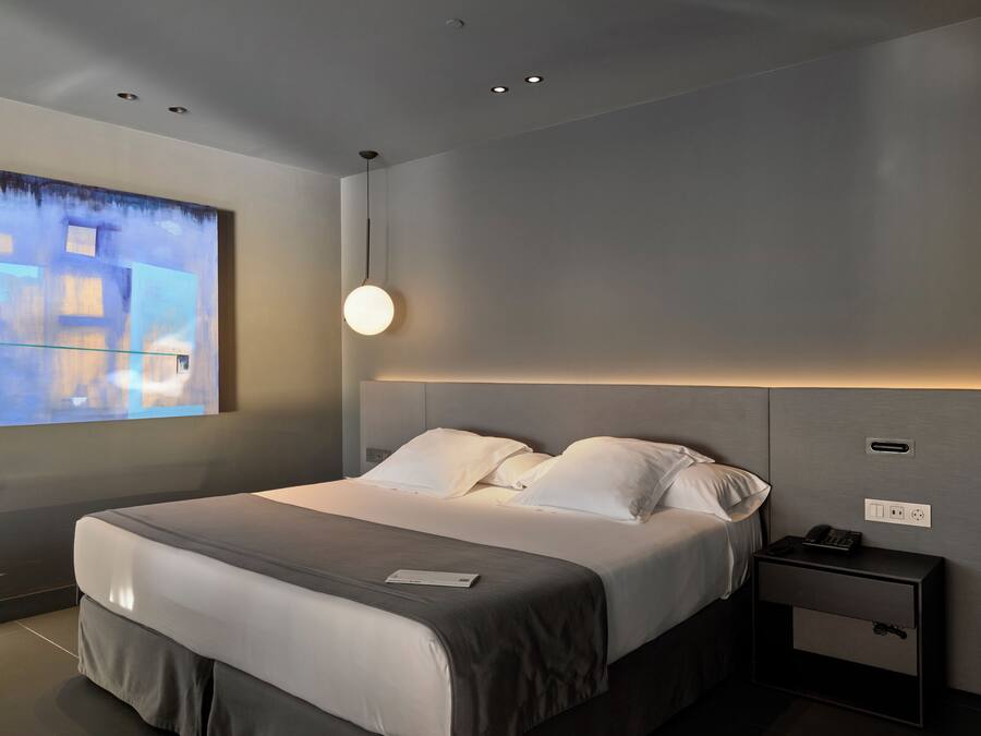 Habitació d'hotel moderna amb un llit gran, una taula de nit i una obra d'art penjada a la paret.