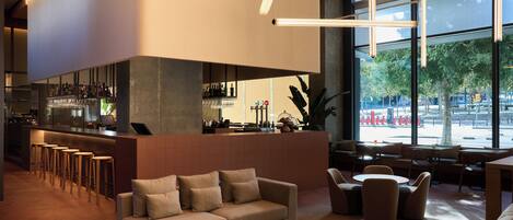 A modern bar area with a sofa and chairs, a bar counter with stools, and large windows offering a view of the outdoors.