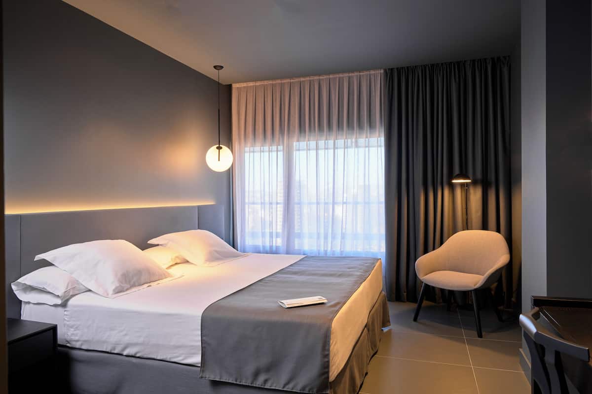 Quarto de hotel moderno com uma cama bem arrumada, uma cadeira e um piano.