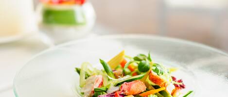 A clear glass bowl of mixed salad with various vegetables and a piece of salmon on a white plate.