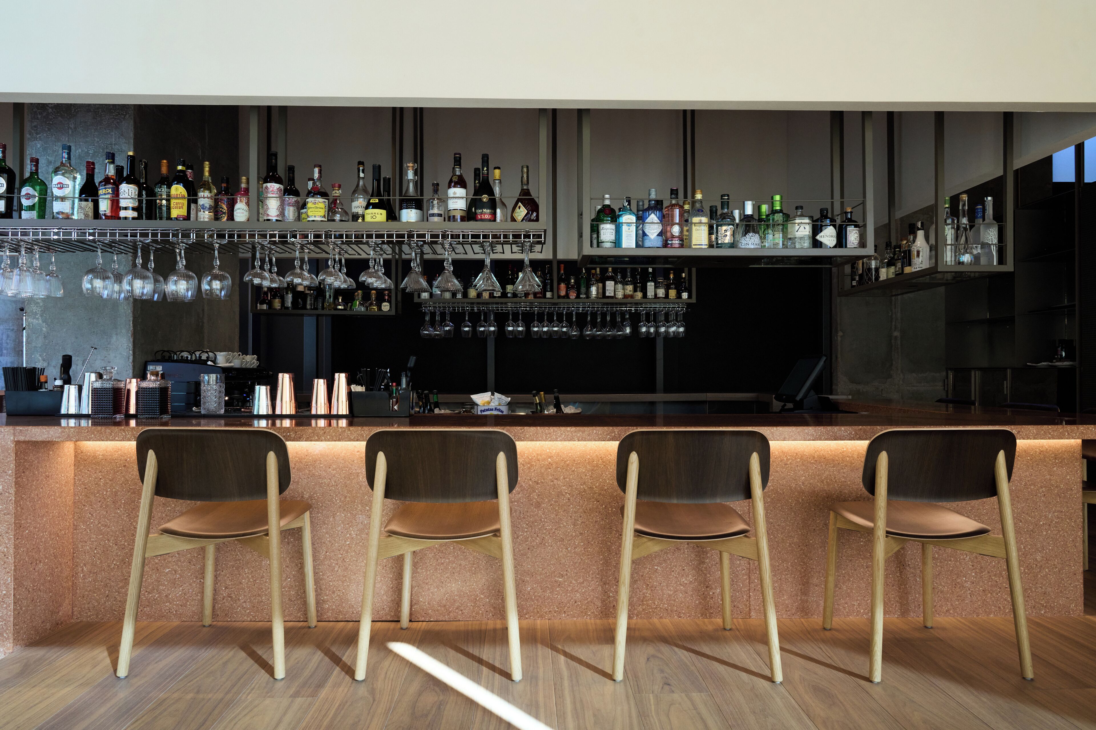 Een bar met een toonbank, verschillende flessenplanken en drie houten stoelen.