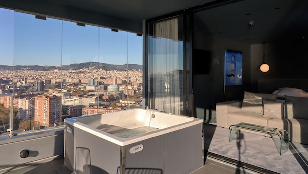 A modern room with a glass bathtub, a sofa, and a city view. - Hotel Barcelona Princess (Barcelona)