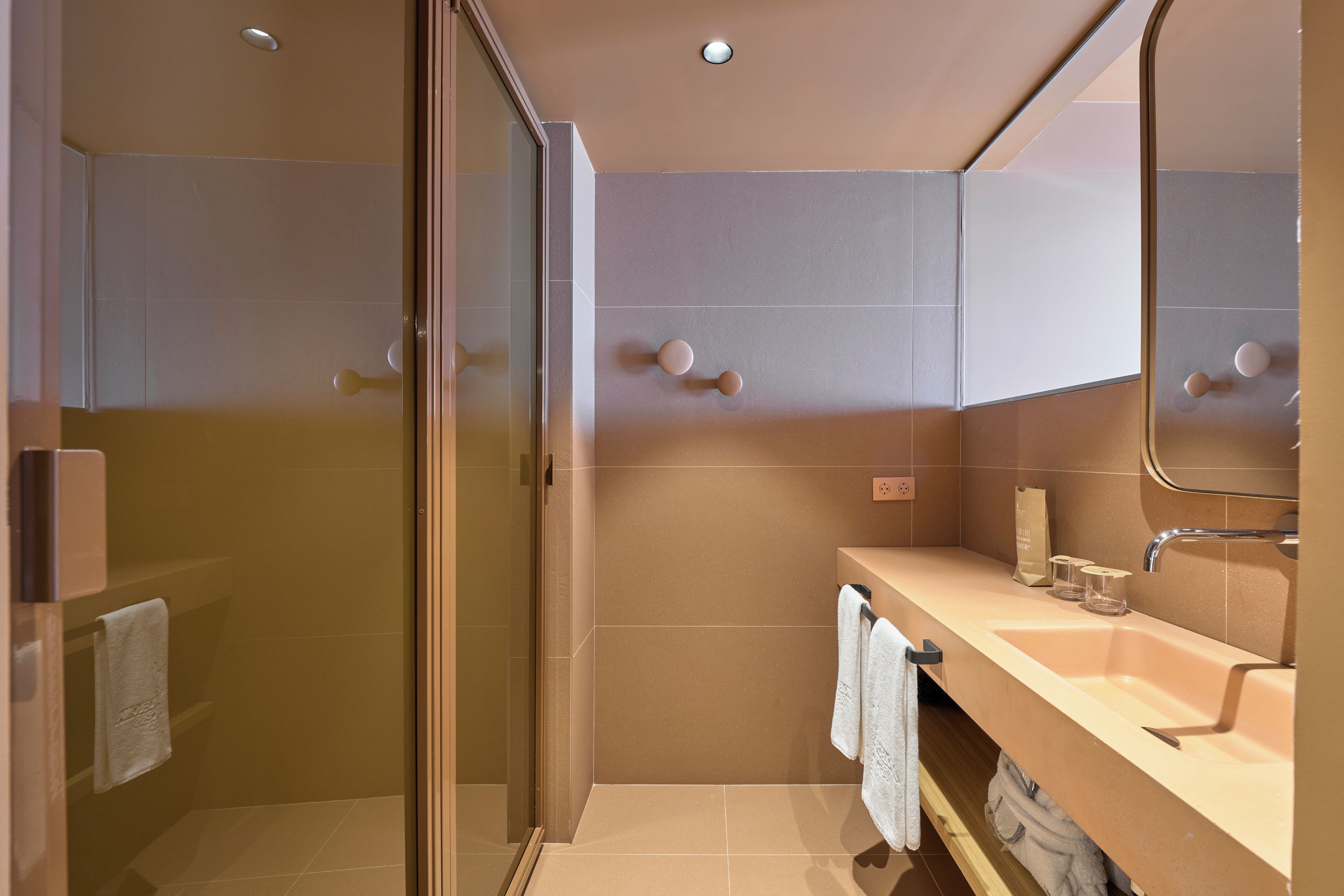 Un bagno moderno con box doccia in vetro, un mobile lavabo color beige e uno specchio grande.