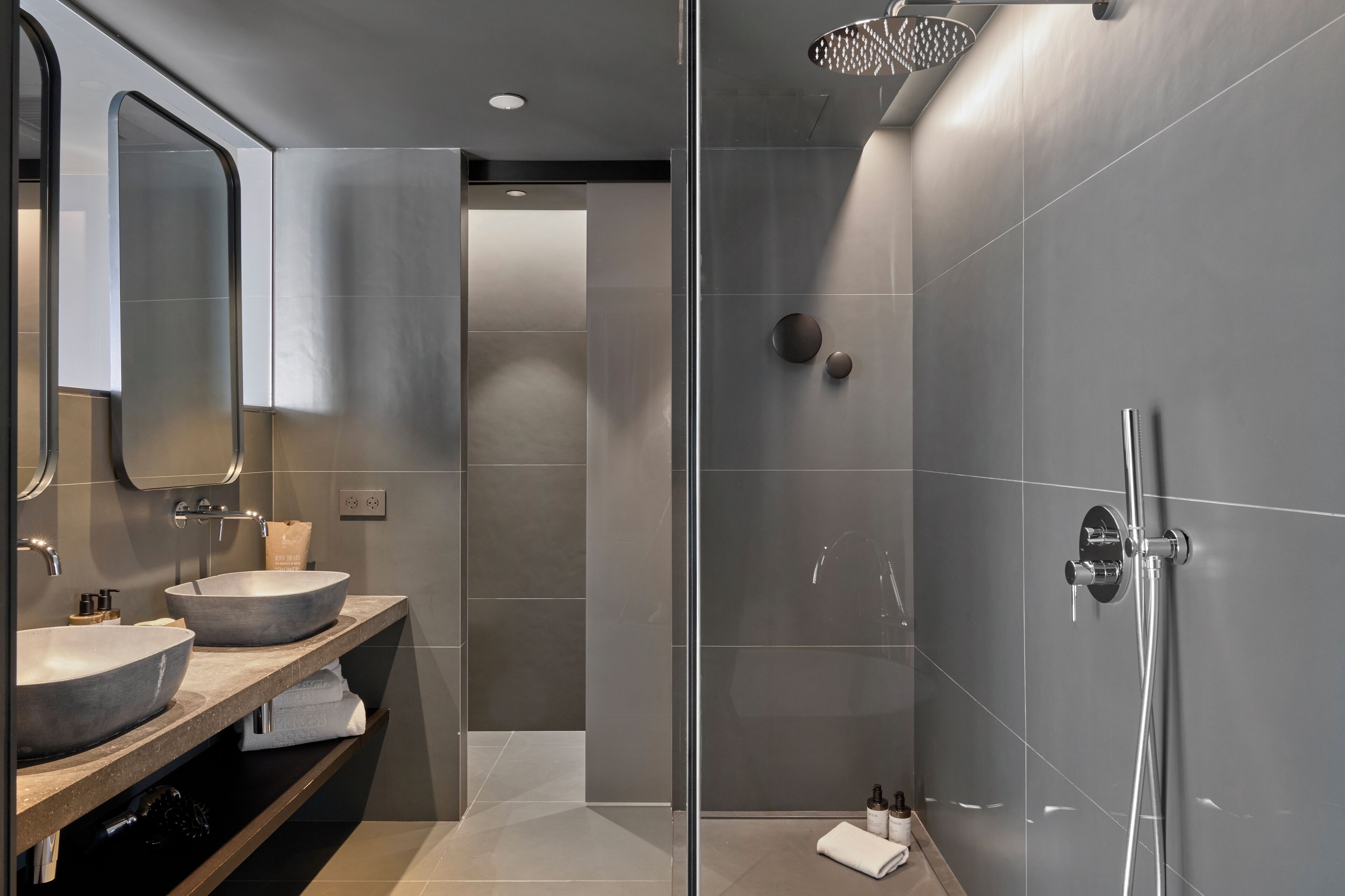 A modern bathroom with two sinks, a large mirror, and a glass-enclosed shower area.