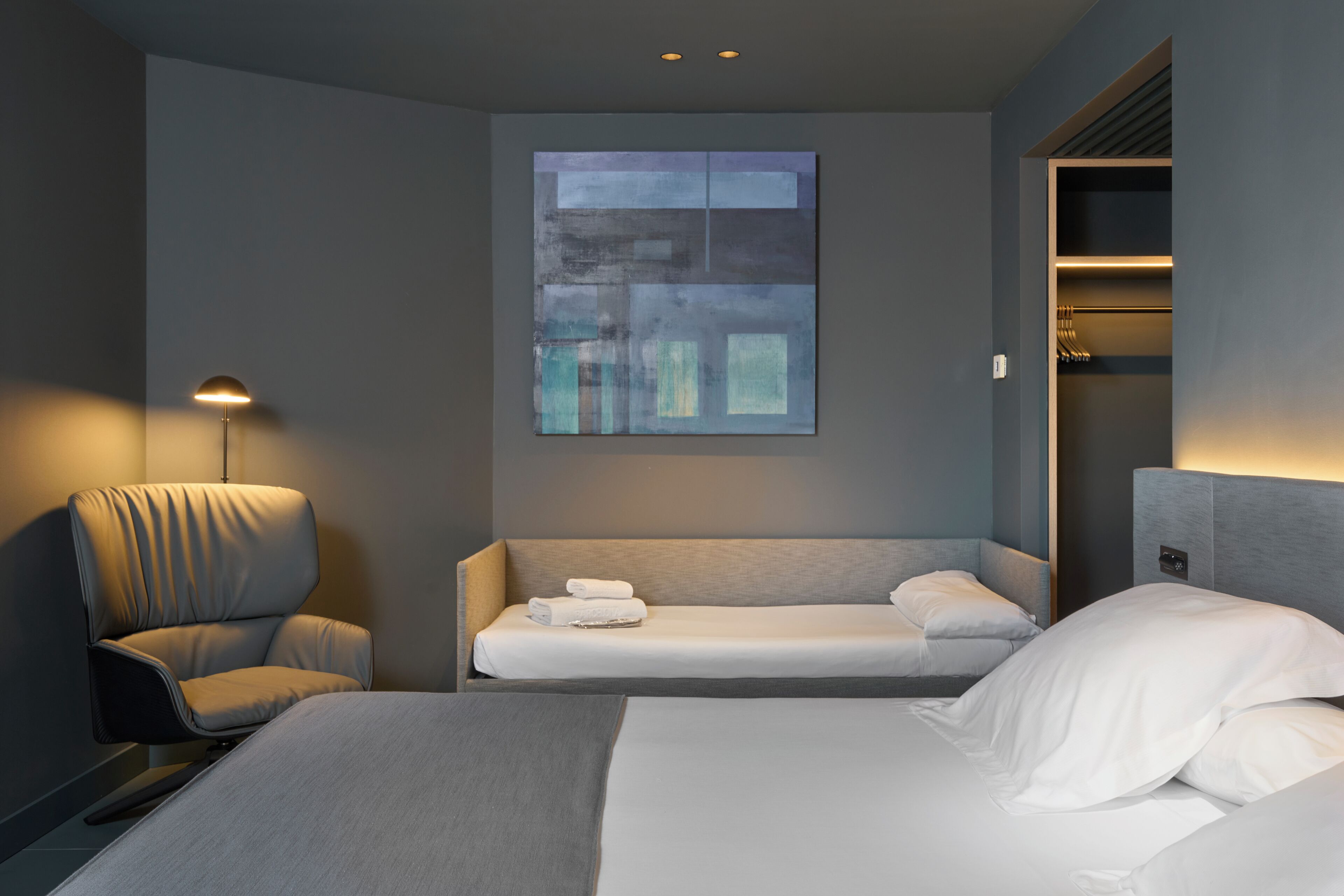 Una habitación de hotel moderna con una cama grande, un sofá, una silla y un televisor montado en la pared.