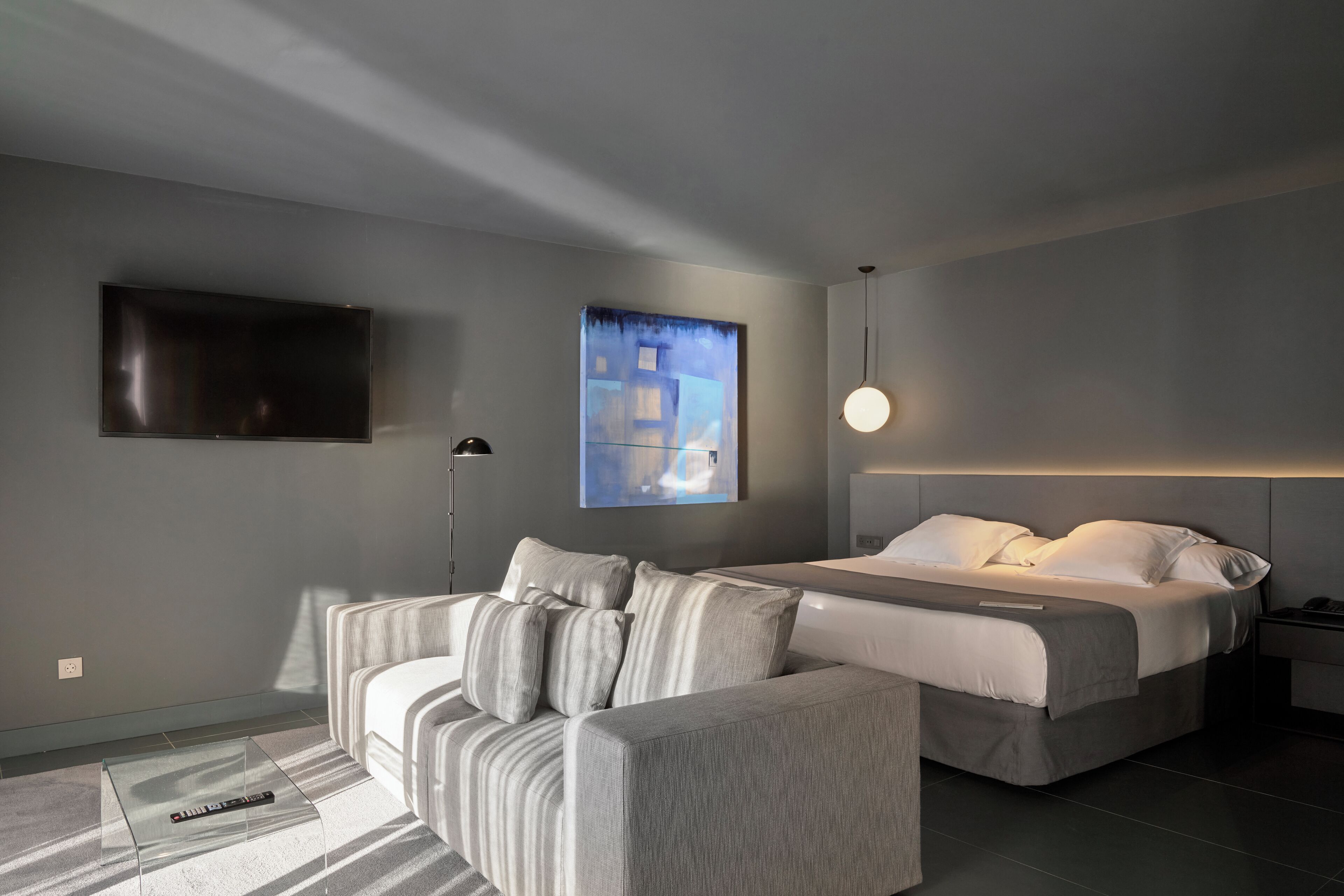 A modern bedroom with a bed, a sofa, a TV, and a painting on the wall.