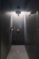 A modern shower with a control panel, a handheld showerhead, and a wall-mounted circular showerhead.