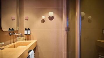 Un baño moderno con un lavamanos color beige, espejo y dos apliques redondos.
