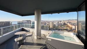 Balcón con jacuzzi, una mesa y sillas, con vista a un paisaje urbano.