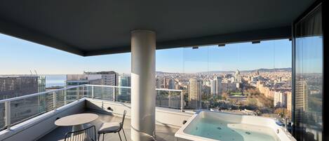 A balcony with a hot tub, a table, and chairs, overlooking a cityscape.