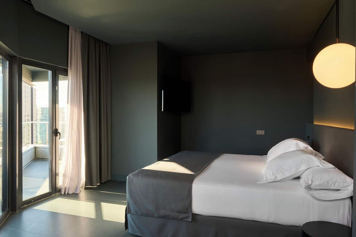 Quarto de hotel moderno com uma cama grande, televisão de tela plana e uma varanda com cortinas.