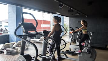 Un gimnasio con cintas de correr y equipo de ejercicio, ventanas amplias y vistas a edificios exteriores.