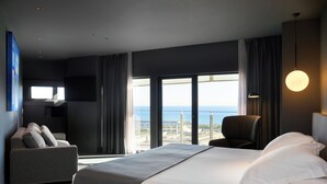 A modern hotel room with a large bed, a sofa, a chair, and a view of the city. - Hotel Barcelona Princess (Barcelona)