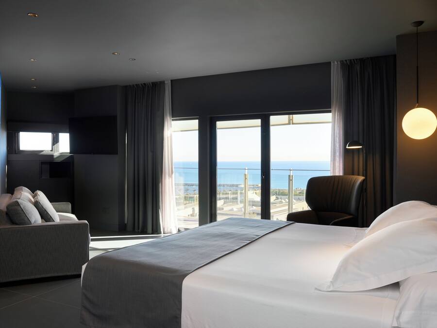 Een moderne hotelkamer met een groot bed, een slaapbank, een fauteuil en uitzicht op de stad.
