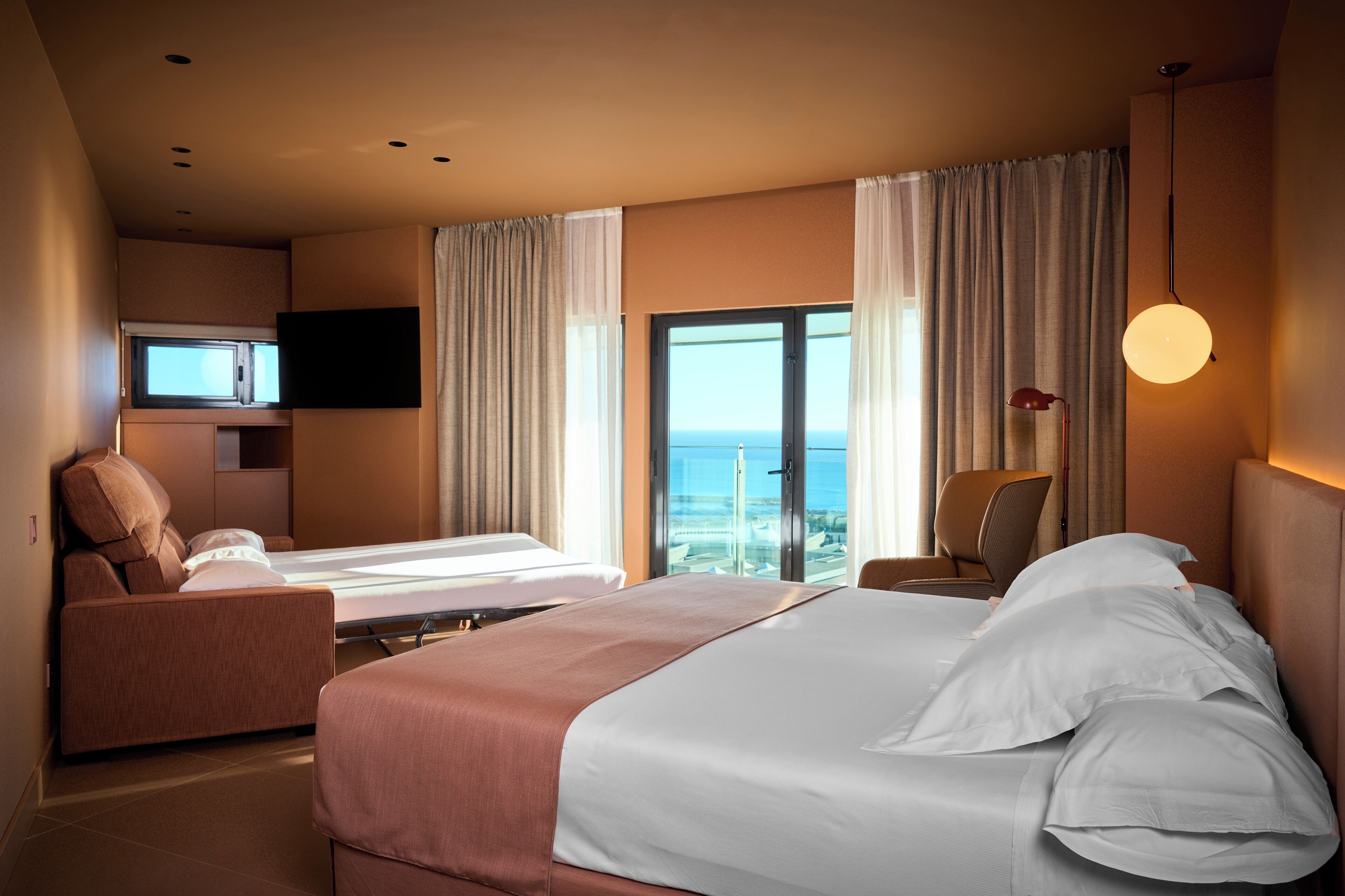 Ein Hotelzimmer mit einem großen Bett, einer Sitzecke, einem Fernseher und Meerblick.
