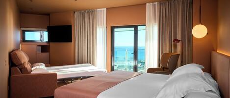 A hotel room with a large bed, a sofa, a TV, and a view of the ocean.
