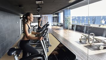 A gym with stationary bikes and a view of a balcony with lounge chairs.