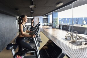 A gym with stationary bikes and a view of a balcony with lounge chairs.