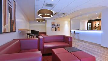 A modern hotel lobby with red leather seating, a bar area, and artwork on the walls.