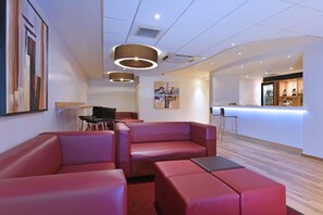 A modern hotel lobby with red leather seating, a bar area, and artwork on the walls. - Travelodge Worcester (Worcester)
