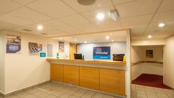 Un comptoir d’accueil avec une enseigne indiquant « Travelodge Worcester », un sol carrelé et une zone recouverte d’une moquette rouge.