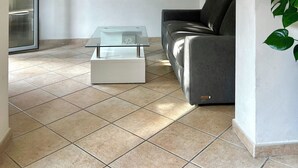 En moderne stue med et glasbord, en grå sofa og to vægmonterede hylder med planter.