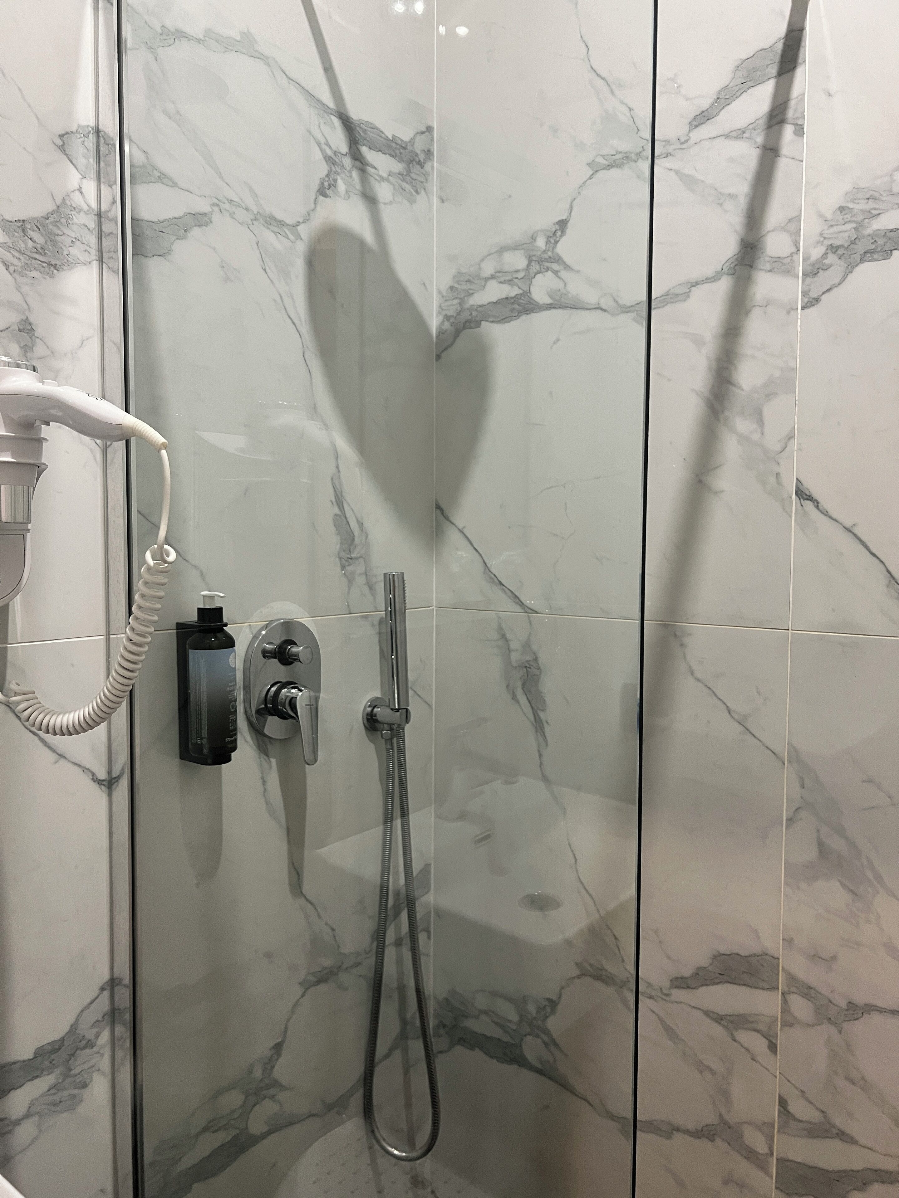 A shower with a handheld showerhead and a wall-mounted control panel.