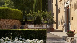 A building with a stone wall, white flowers, and a mountain in the background. - Son Brull Hotel & Spa (Pollenca)