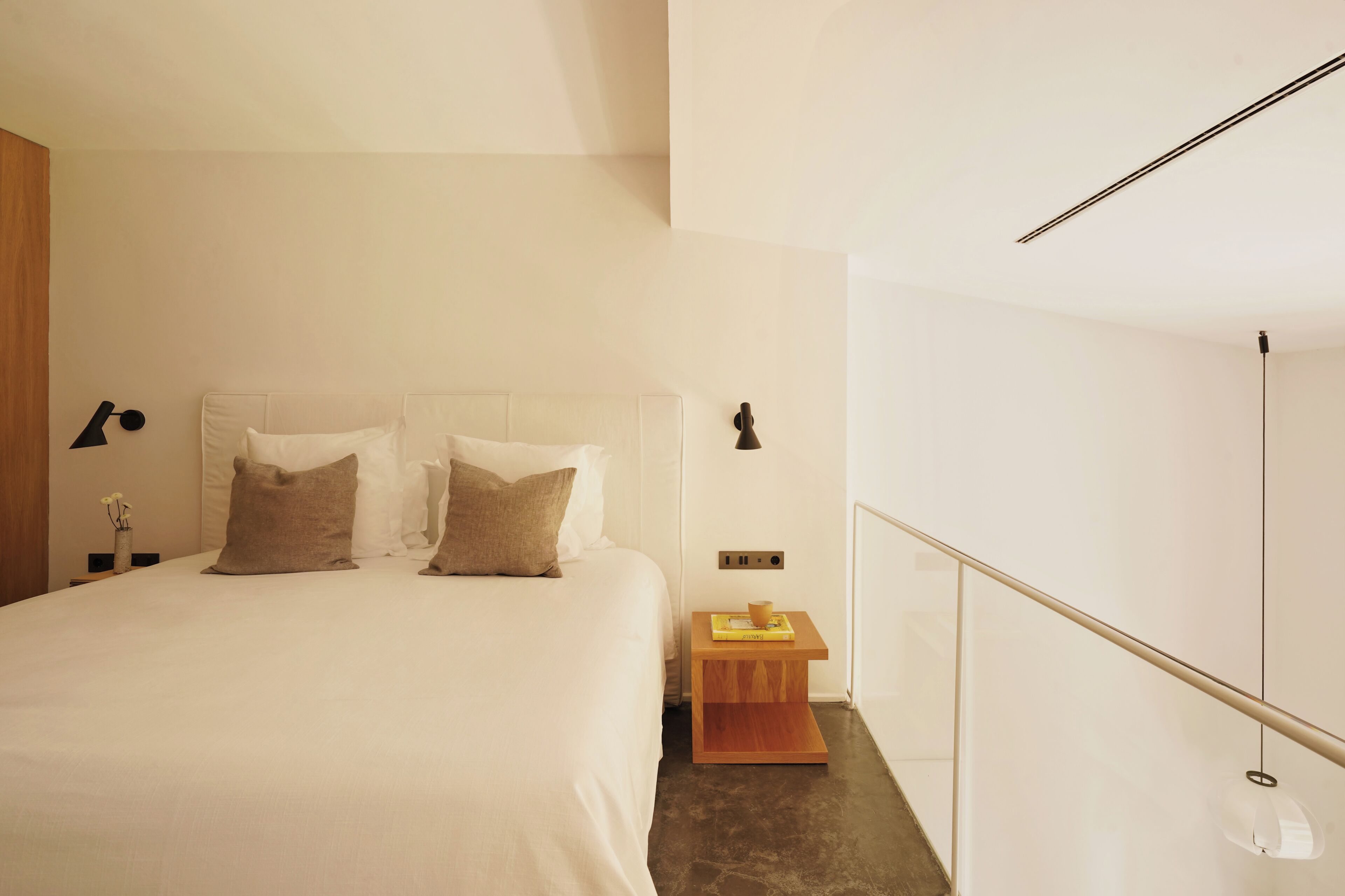 Un dormitorio minimalista con una cama grande, dos mesitas de noche y una pequeña mesita auxiliar de madera.
