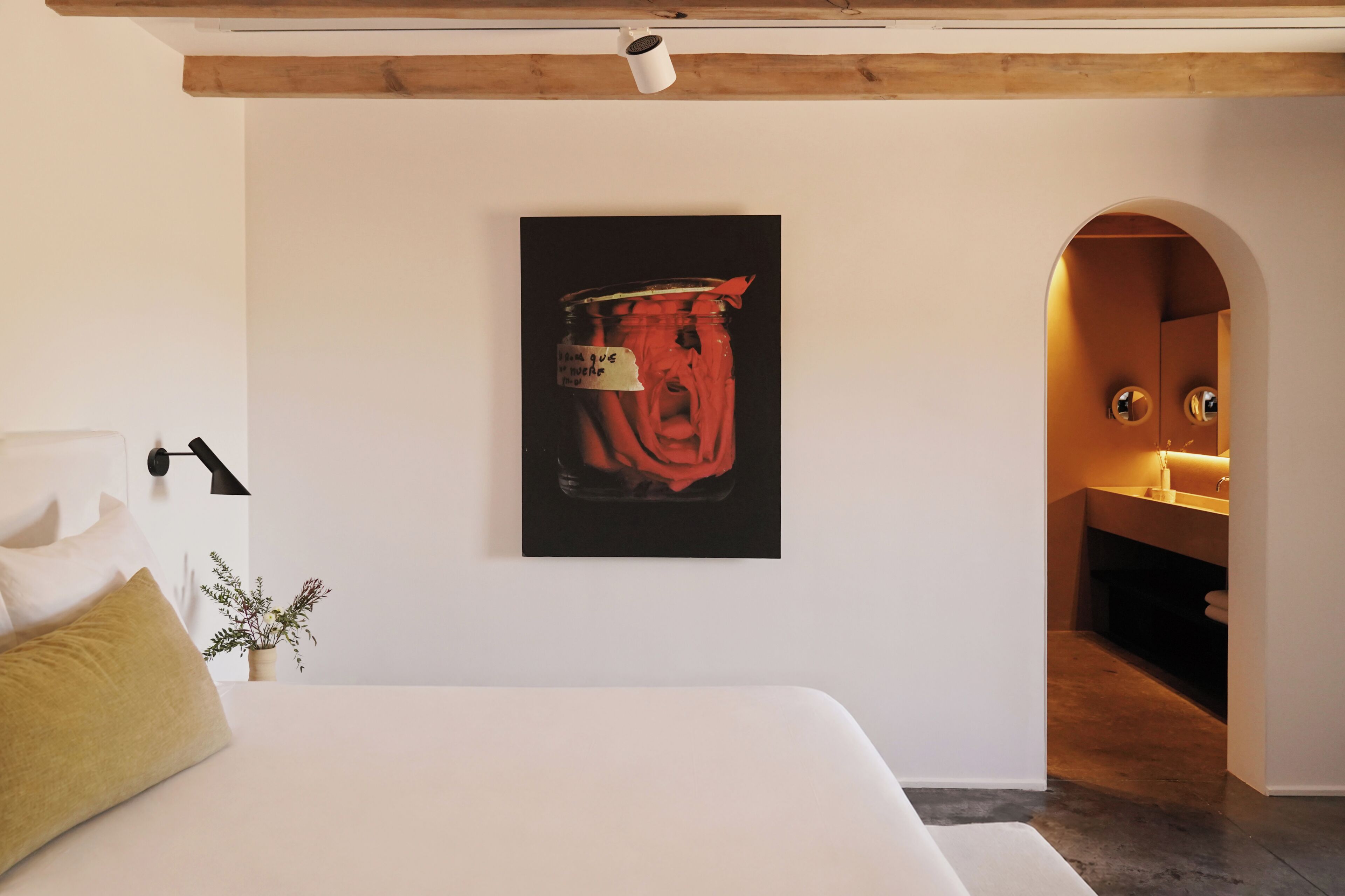 A bedroom with a bed, a nightstand, a lamp, a potted plant, and a wall-mounted artwork.