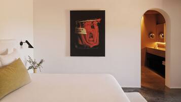 A bedroom with a bed, a nightstand, a lamp, a potted plant, and a wall-mounted artwork.