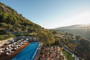A poolside area with lounge chairs and tables, surrounded by greenery and hills. - Son Brull Hotel & Spa (Pollenca)