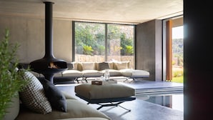 A modern living room with a fireplace, comfortable seating, and a large window offering a view of greenery. - Son Brull Hotel & Spa (Pollenca)