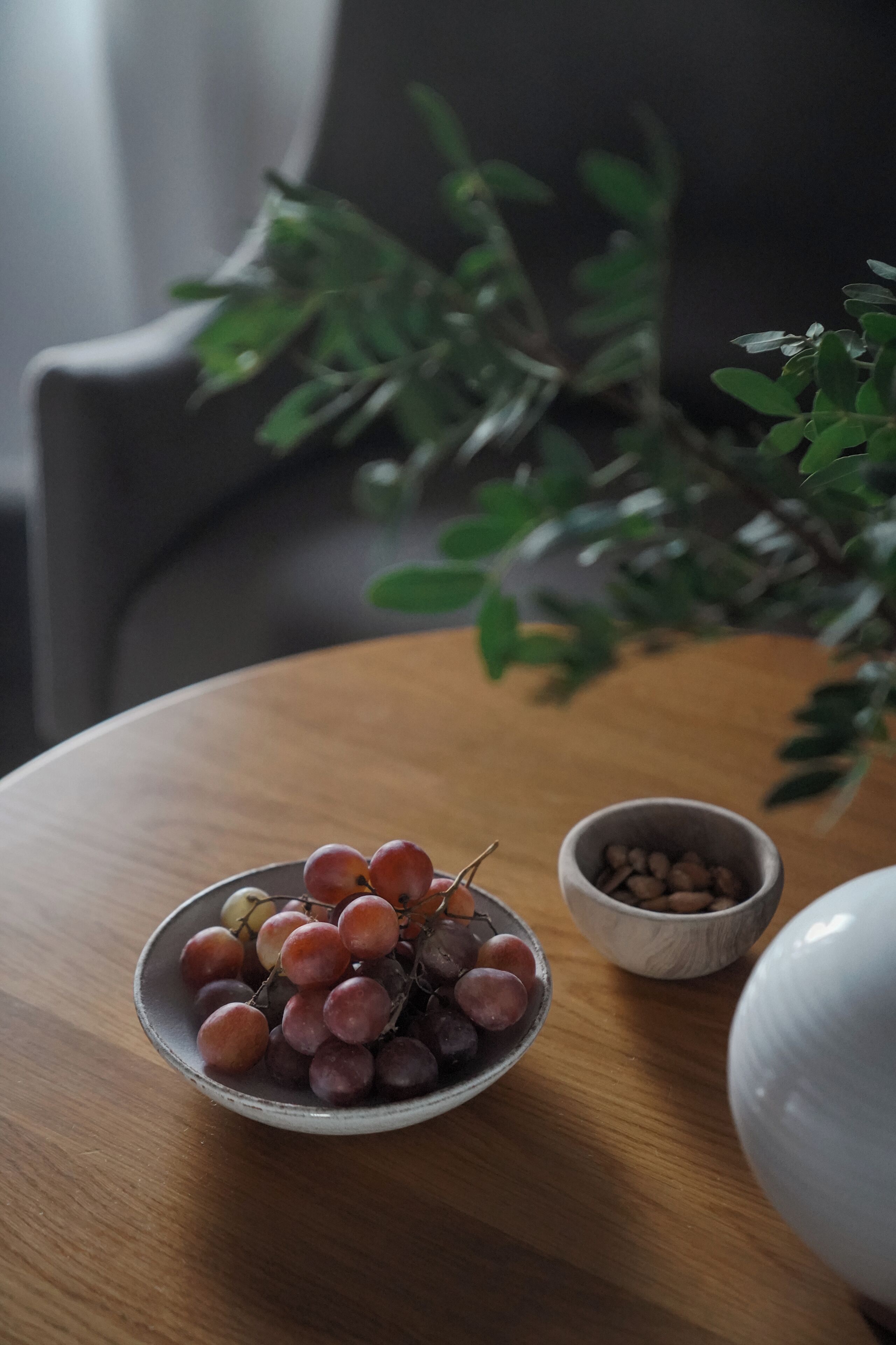 Una mesa de madera redonda con un cuenco de uvas y un tazón pequeño de granos de café.