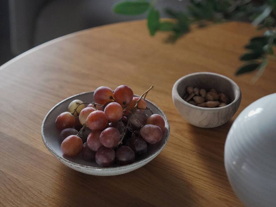 Una mesa de madera redonda con un cuenco de uvas y un tazón pequeño de granos de café.