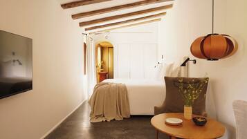 Habitación de hotel moderna con cama, televisión, mesa de comedor con un tazón, una silla y una lámpara colgante.
