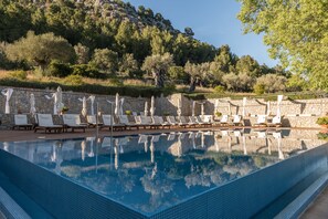A swimming pool with lounge chairs and umbrellas, surrounded by stone walls and trees. - Son Brull Hotel & Spa (Pollenca)