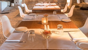 A dining area with a long table set for four, stone walls, and a hanging light fixture. - Son Brull Hotel & Spa (Pollenca)