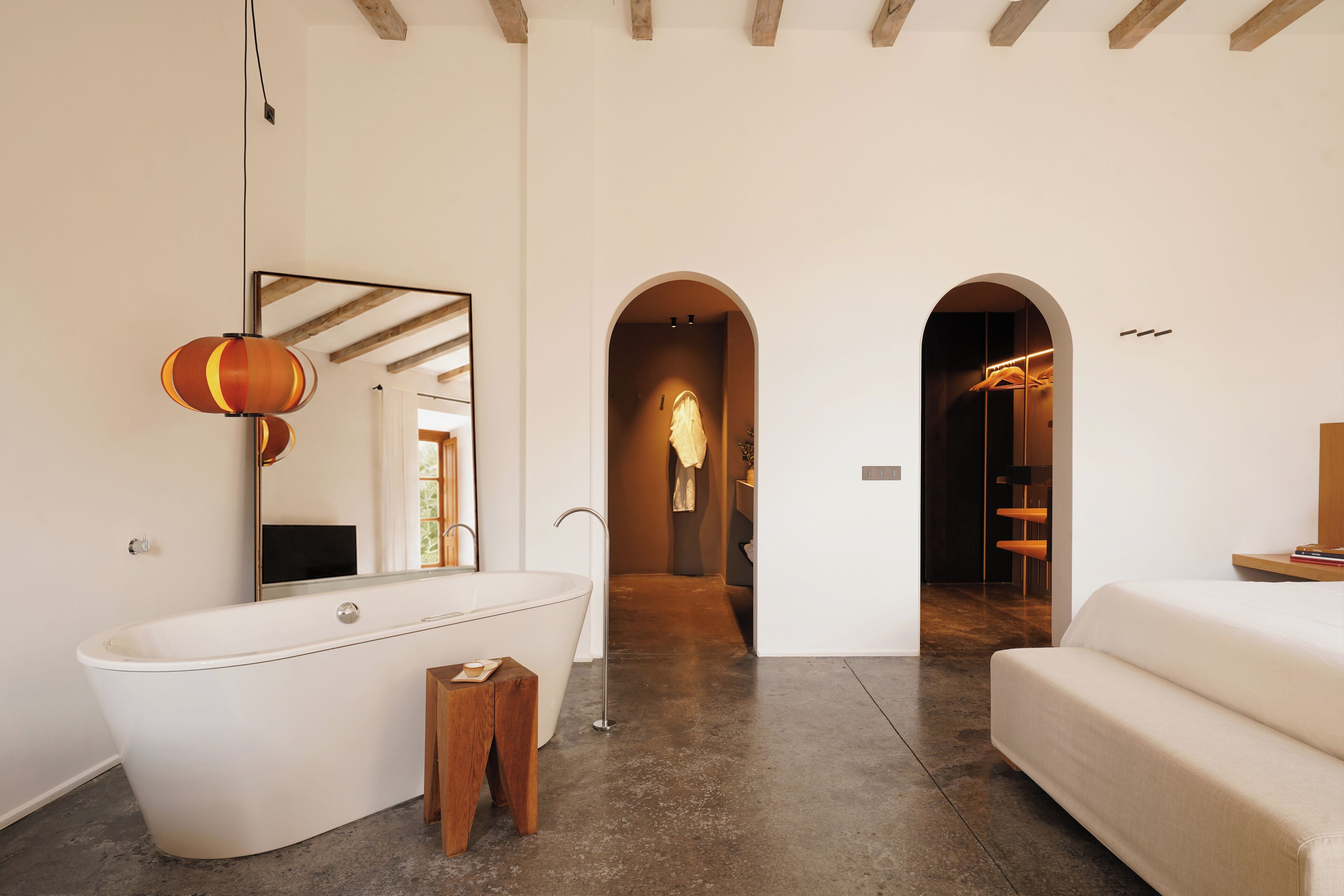 A modern bathroom with a freestanding bathtub, a wooden stool, and a large mirror.