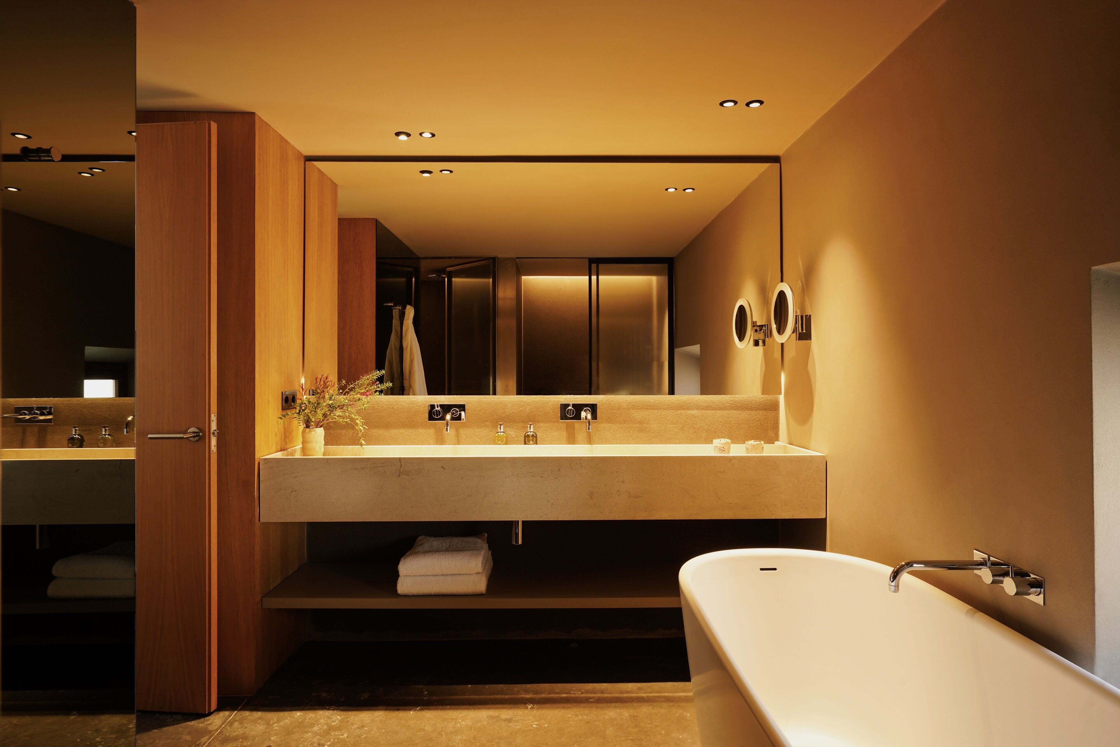 Un baño moderno con una bañera independiente, un tocador amplio con un espejo e iluminación empotrada en el techo.