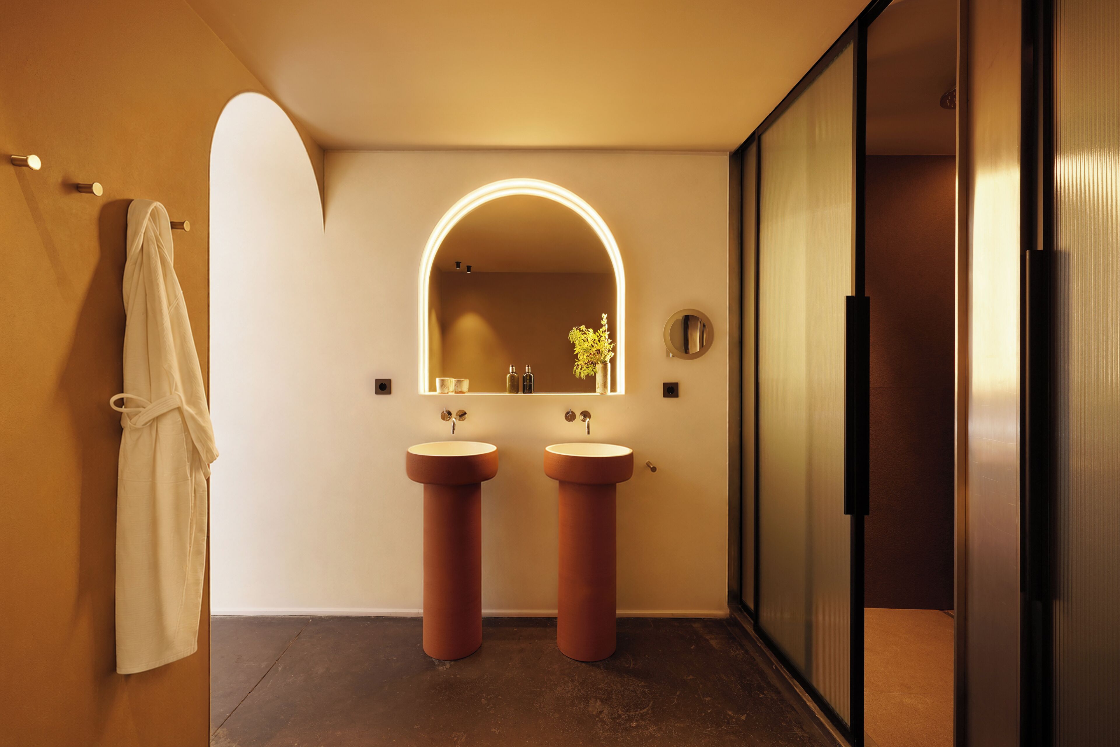A modern bathroom with two sinks, a large mirror, and a robe hanging on the wall.