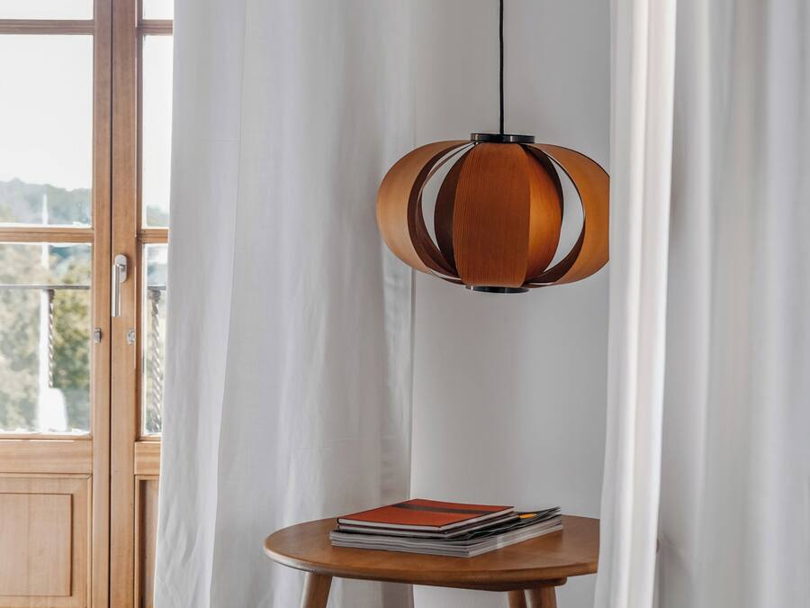 Una habitación con puerta de madera, cortinas blancas, una mesa redonda con una pila de libros y una lámpara colgante.